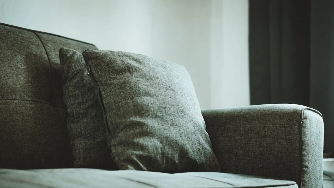Grey fabric cushion and upholstered sofa showing woven textile texture